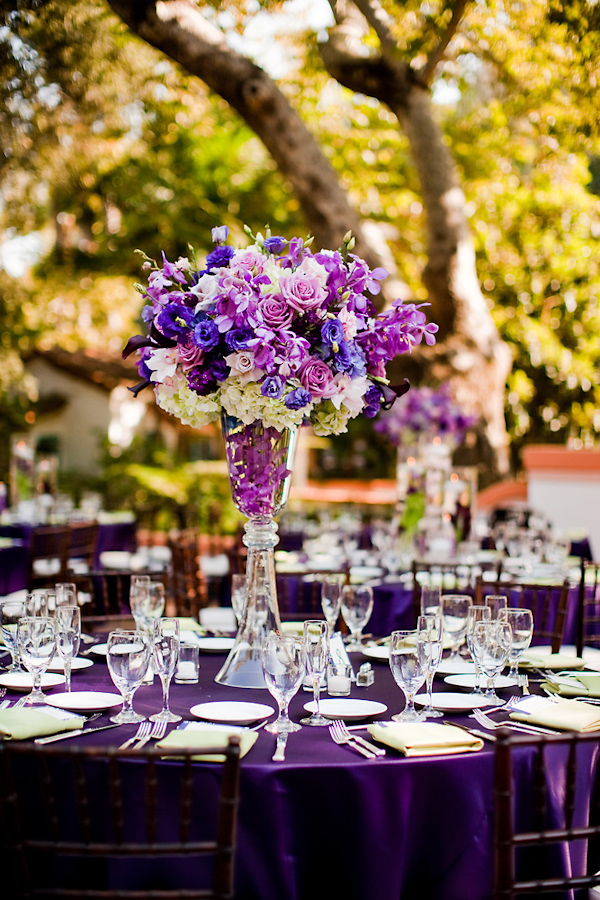 Table setting at outdoor reception - Purple tablecloth with purple, lavendar, ivory, and dark blue floral centerpiece - wedding photo by Michael Norwood Photography